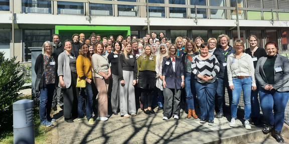 Many people in colorful clothing stand in front of a building at the Technical University of Dortmund.en Universität Dortmund.