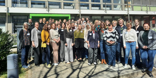 Viele Menschen in bunter Kleidung stehen vor einem Gebäude der Technischen Universität Dortmund.