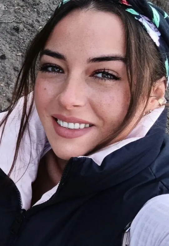 Nahaufnahme einer lächelnden Frau mit dunklen Haaren, die ein bunt gemustertes Haarband trägt und eine dunkle Jacke über einem hellen Oberteil.
