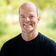 Dr. Harald, bald man wearing a black T-shirt, standing outdoors with a blurred green background.
