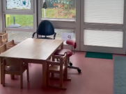 Children's table with several small chairs in front of a glass door with colorful window decorations and partially closed blinds