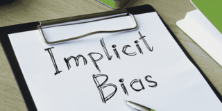 Schreibblock mit der handschriftlichen Aufschrift 'Implicit Bias' und einem Kugelschreiber auf einem Tisch