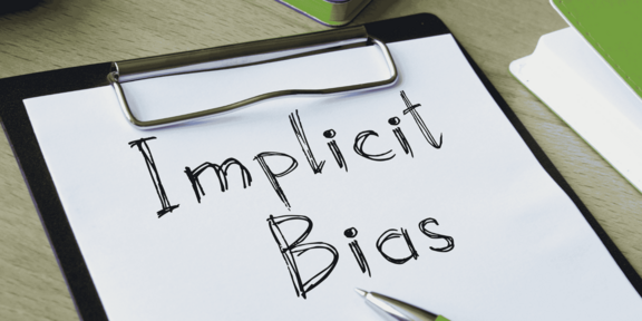Schreibblock mit der handschriftlichen Aufschrift 'Implicit Bias' und einem Kugelschreiber auf einem Tisch