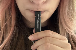 Person holds a rectangular emergency whistle with visible text "SchuDS" to their mouth.
