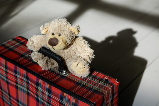 kleiner Koffer, auf dem ein Teddybär sitzt