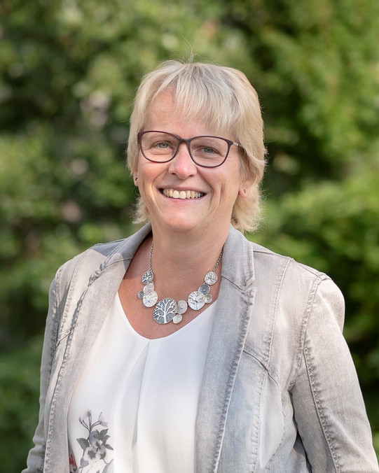 A female person with blond hair and glasses.