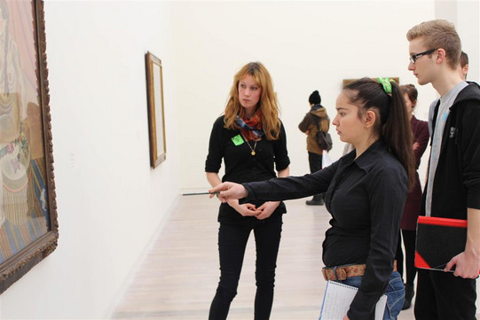  A woman points a magic wand at a picture, with a woman and a man standing around it 