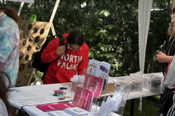 Tent with a table displaying informational materials and buttons, people in the background