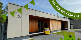 Modern building with wooden cladding and gray facade, small yellow-and-white vehicle in front, green bunting and 'Tag der offenen Tür' text.