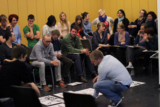 People sit in their seats, a man bends over pictures