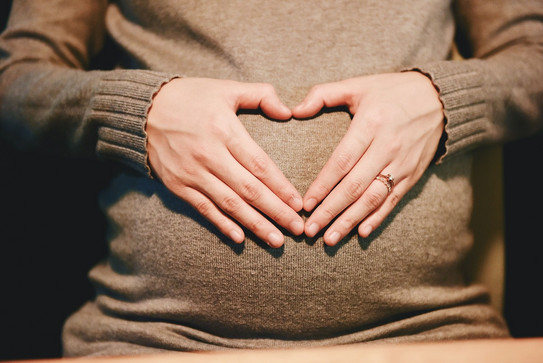 A woman places her hands together like a heart on her pregnant belly. 