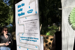 Poster titled 'Ride the Leaky Pipeline' attached to a gray pole outdoors with people and trees in the background.