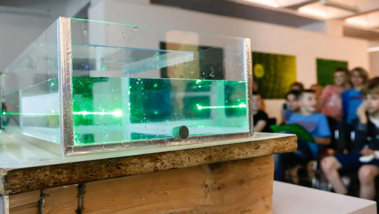 Transparent rectangular container with green laser light and a blurred group of children in the background