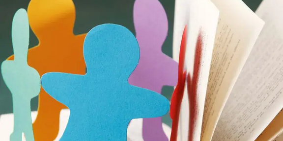 Several colorful paper figures in human form are standing side by side in front of an open book