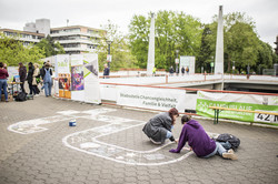 Zwei Personen sitzen auf dem Boden und malen mit Kreide das TU Logo aus.