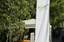 Tall white banner with the text 'queer peers' next to a tree and an outdoor canopy.