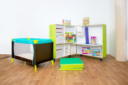 Im Vordergrund ein Reisebett für Kinder, daneben eine Gymnastikmatte, dahinter die grüne KidsBox geöffnet