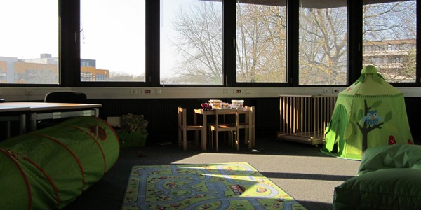 Eltern-Kind-Raum mit Spielzelt und Tunnel in grün und einem Kindertisch und Laufstall im Hintergrund