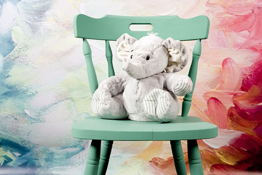 A stuffed elephant is sitting on a green chair in front of a colorful background