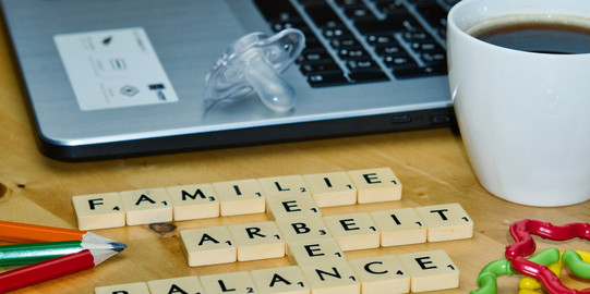 Symbolbild Dual Career Laptop, Kaffeetasse, Stift, Schnuller, Beißring und Slogan "Familie, Leben, Arbeit, Balance"
