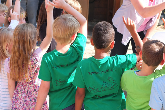 Eine Gruppe von Kindern mit grünen T-Shirts sind von hinten zu sehen und melden sich.