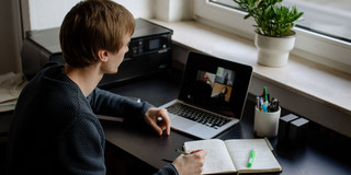 Ein Student arbeitet mit Laptop und Notizbuch.