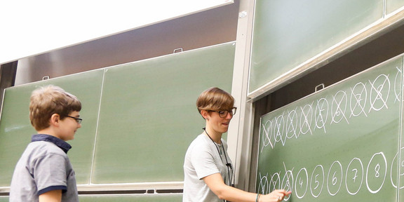 Lecturer and a young boy are standing in front of a blackboard