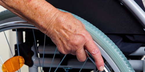 Close-up of an old hand holding a wheel of a wheelchair.
