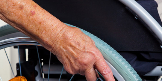 Detailaufnahme Hand eines Seniors am Rollstuhlrad